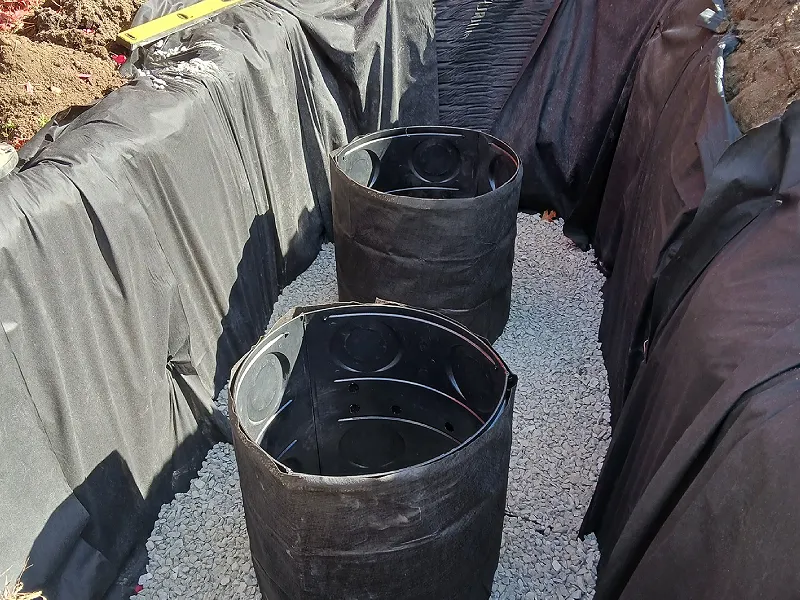 Drainage installation featuring black barrels surrounded by landscaping fabric and gravel, illustrating a professional drainage solution by Cut Above Landscaping Inc.