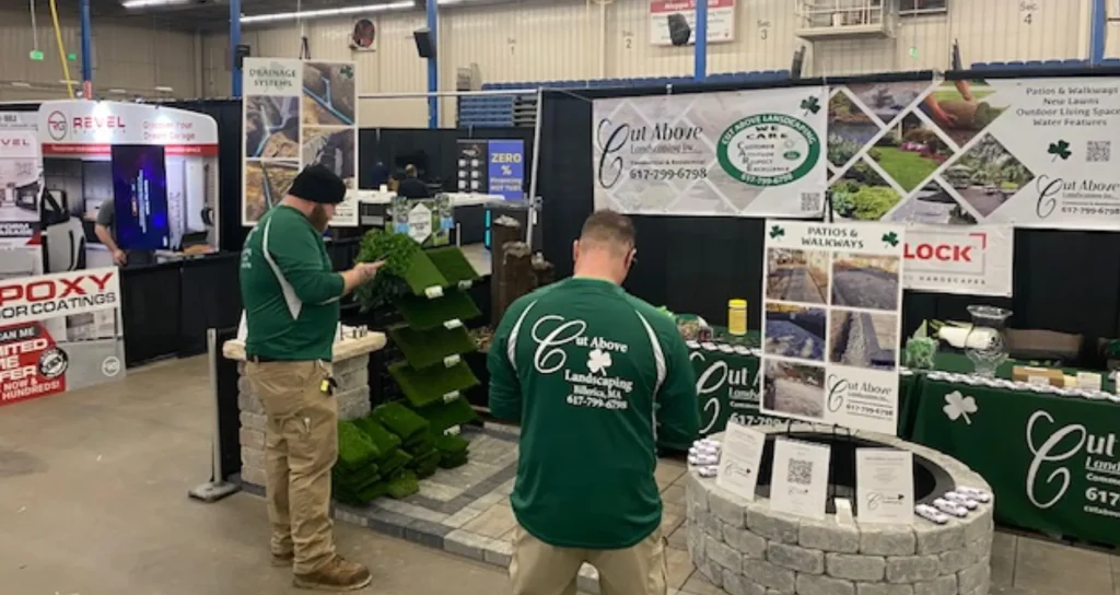 Cut Above Landscaping Inc. booth at Suburban Boston Home Show featuring staff engaging with artificial grass displays and promotional materials, showcasing landscaping services and project highlights.