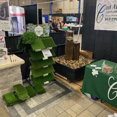 Cut Above Landscaping Inc. display with artificial turf, fountain, and Unilock pavers at a home show.