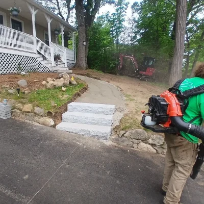 Cut Above Landscaping worker blowing debris near granite steps and Unilock paver walkway installation.