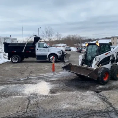 Bobcat and Ford truck in a commercial snow management setting, applying salt and ice melt on a snowy parking lot, ensuring winter safety and accessibility.