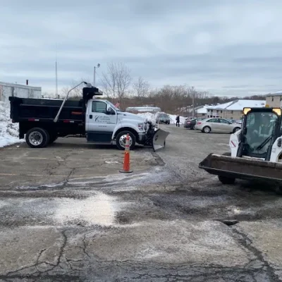 Commercial snow management vehicles, including a Ford truck with a plow and a Bobcat loader, on a snow-covered parking lot, demonstrating effective snow removal and safety measures for winter operations.