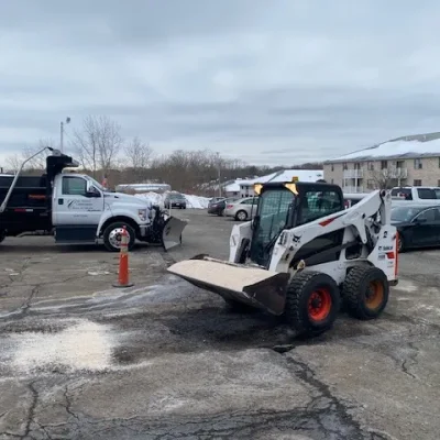 Bobcat applying salt in a commercial parking lot for snow management, with a Ford truck equipped for snow removal in the background, ensuring winter safety and accessibility.