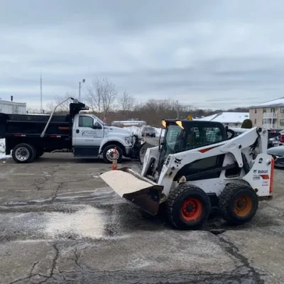 Bobcat snow removal equipment and Ford truck in a snowy commercial parking lot, showcasing winter maintenance services for safe surfaces and accessibility.